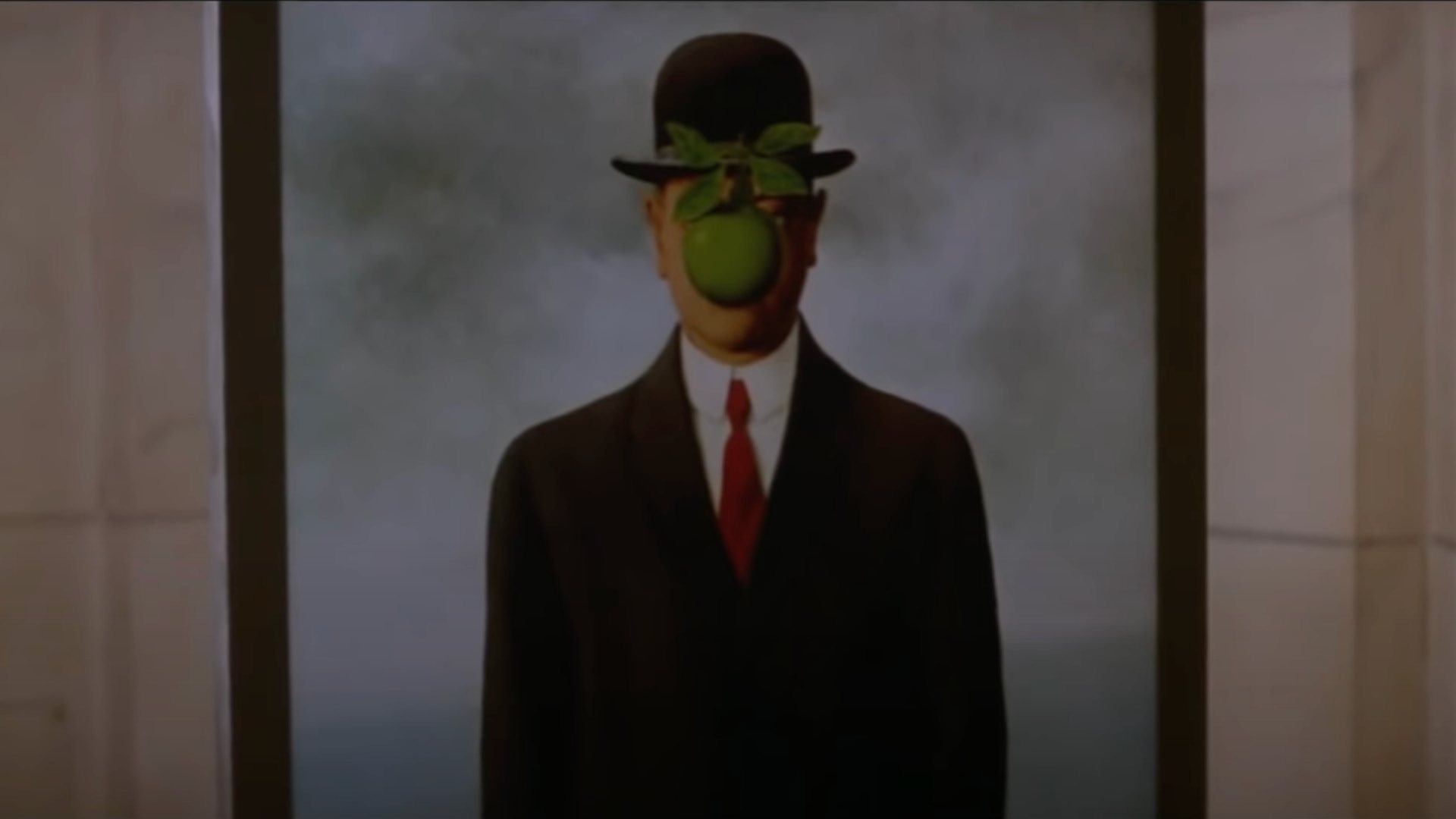THE THOMAS CROWN AFFAIR film still of man in a suit, red tie, and black hat with a green apple in front of their face.