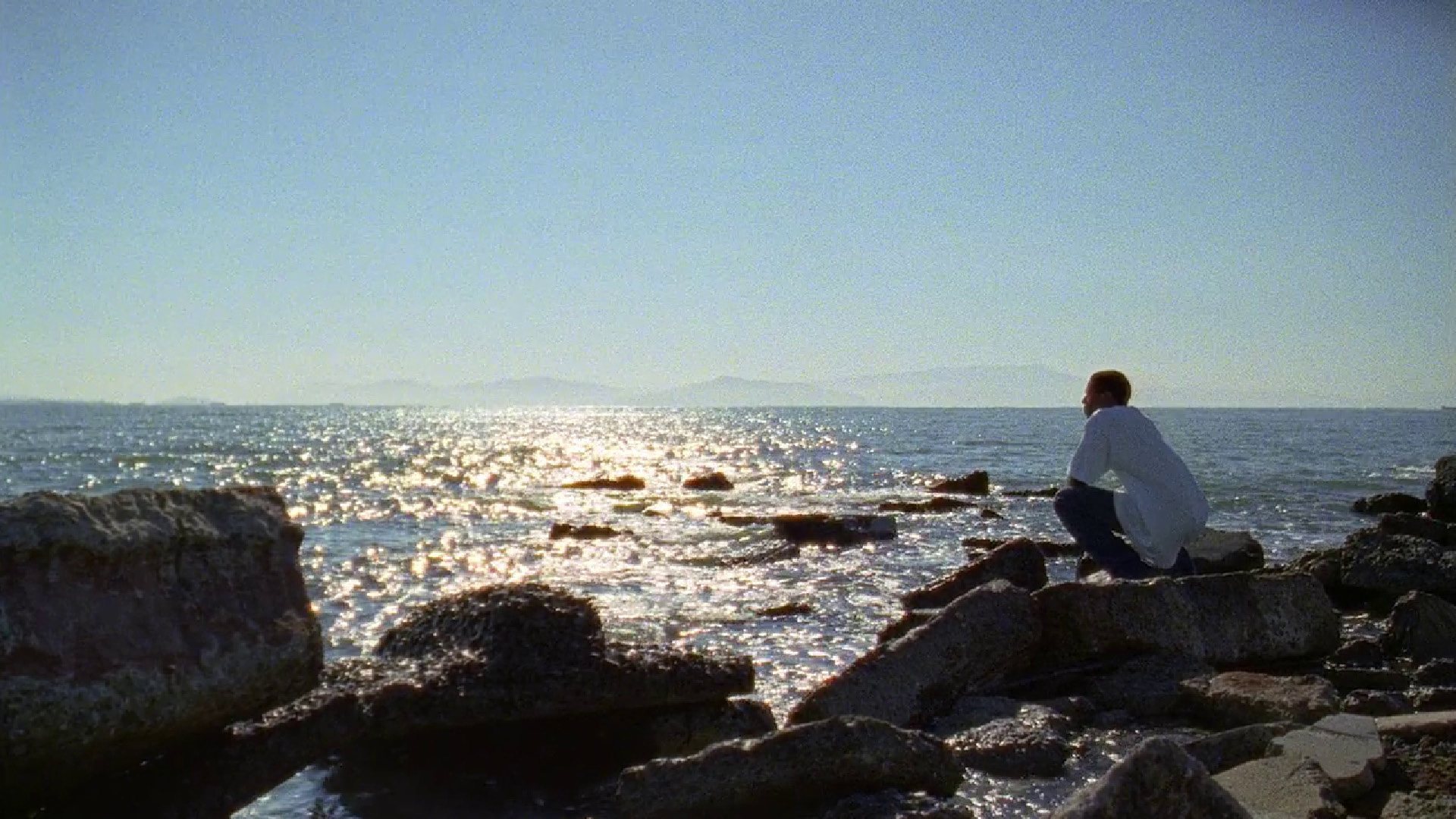 FRUITVALE STATION film still of Michael B. Jordan crouching on rocks near the ocean