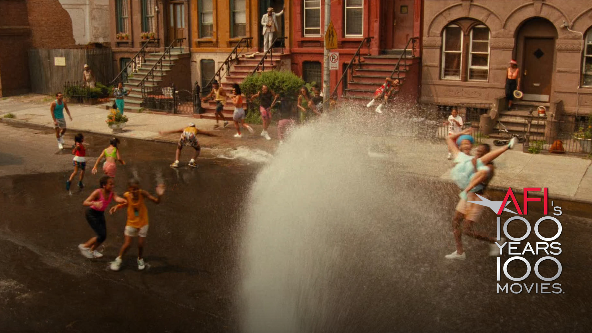 On the right corner is the AFI 100 YEARS...1000 MOVIES logo. Film still from DO THE RIGHT THING: On a blistering hot summer day in Brooklyn, residents of a brownstone-lined street play in the water shooting our from a fire hydrant.
