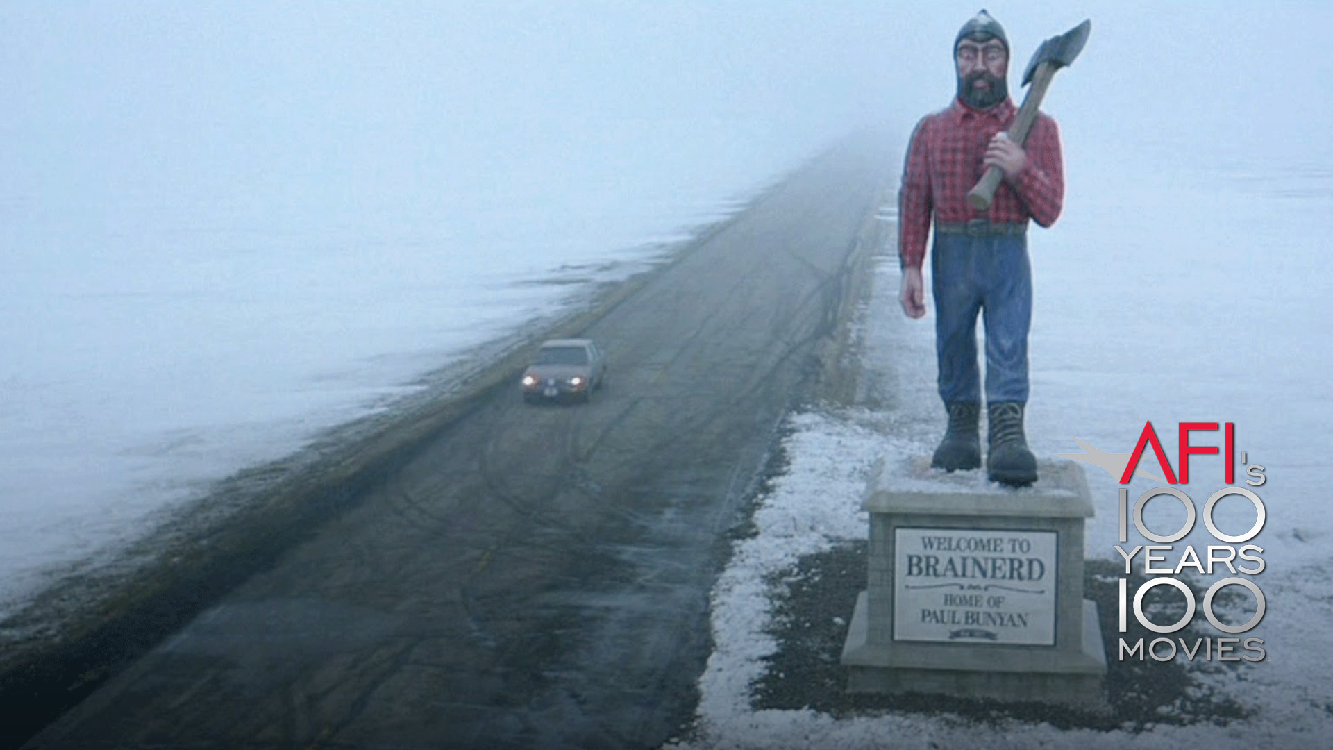 On the right corner is the AFI 100 YEARS...100 MOVIES logo. The film still is from FARGO: The image -- a wide shot taken from high above the ground) shows a Paul Bunyan statue on the side of a road. Snow covers the ground on either side of a road. A lone car drives toward the camera.
