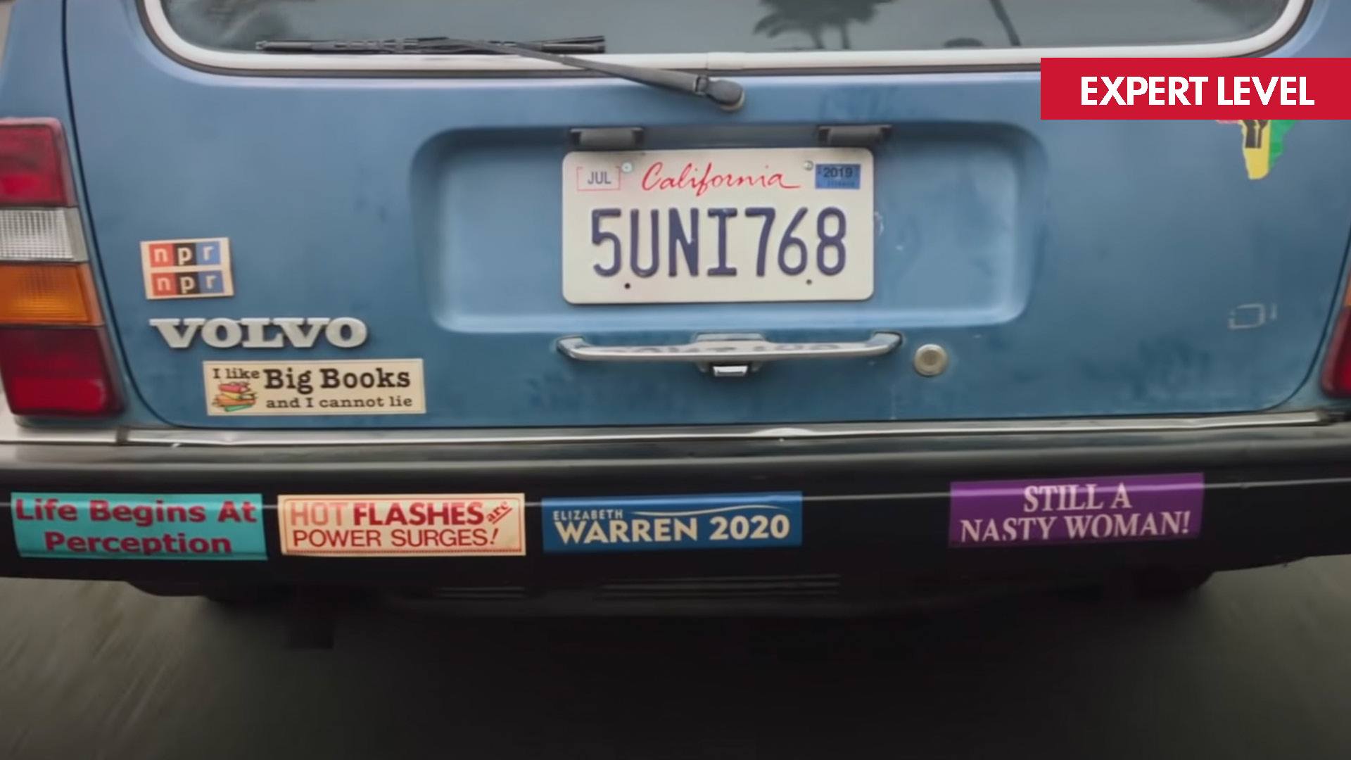 Film still from movie BOOKSMART - the back of a old blue Volvo. The black bumper is covered with bumper stickers.